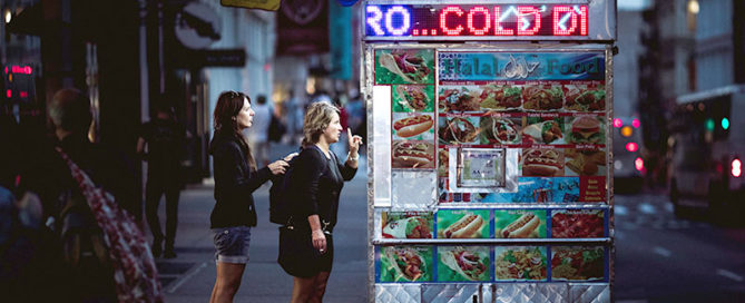 Two women order from a sidewalk vending shop